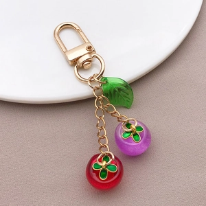 Detail of cherry-shaped keychain with red and purple beads and golden D-ring clasp