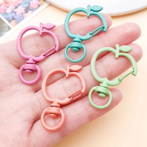 Handheld view of apple-shaped lobster clasps in assorted macaron paint colors for DIY
