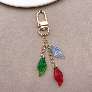 Detail view of colorful glass leaf pendants on a golden keychain on grey fabric