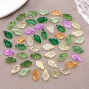Colorful leaf shaped glass beads for DIY jewelry making laid on textured fabric