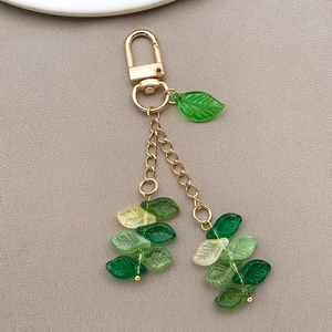 Detailed macro view of green glass leaf charms with gold lobster clasp and lifelike veins