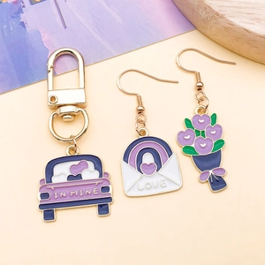 Vista plana de llavero de coche esmaltado morado y pendientes de corazón asimétricos