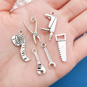 Macro view of six antique silver tool charms including a drill and wrench held in hand