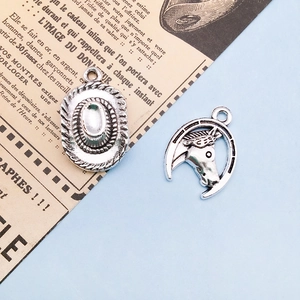 Detail of silver cowboy hat and horseshoe charms for DIY jewelry on vintage paper