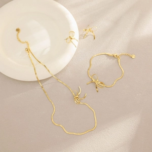 Parure collier et boucles d'oreilles nœud doré sur assiette en céramique blanche