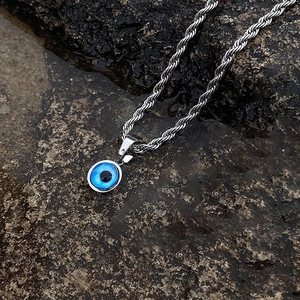 Detailed macro shot of an evil eye pendant on a rugged rope chain over wet stone