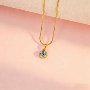 Detail of blue evil eye pendant on a gold snake chain with soft pink background