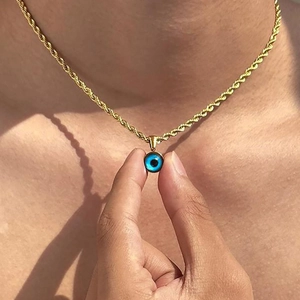 Golden rope chain necklace with a blue evil eye pendant worn on a sunlit background