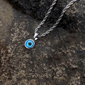 Blue evil eye pendant necklace with silver rope chain on a natural dark rock background