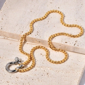 18k gold plated box chain necklace with silver D-shackle buckle on travertine surface