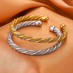 Dettaglio di bracciali a fune intrecciata in oro e argento su tessuto di raso champagne