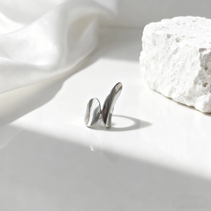 Detalle de anillo geométrico de titanio pulido sobre piedra blanca con tela de seda