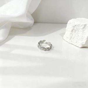 Anillo abierto minimalista de hoja de olivo en acero plateado sobre fondo de seda blanca