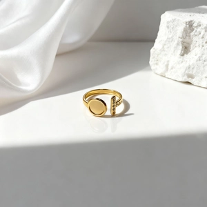 Detalle de anillo dorado ajustable con diseño ovalado hueco y circonitas sobre seda blanca
