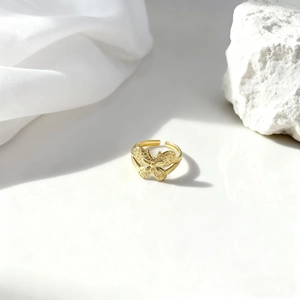 Detalle del anillo de mariposa dorado calado sobre seda blanca y piedra texturizada