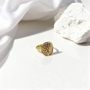 Detalle de anillo dorado vintage con grabado de sol sobre tela de seda blanca pura