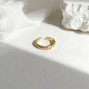Anillo dorado ajustable con textura trenzada y diseño ovalado sobre fondo de piedra