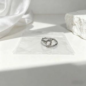 Anillo ovalado plateado con diseño de metal líquido sobre seda blanca y piedra pura