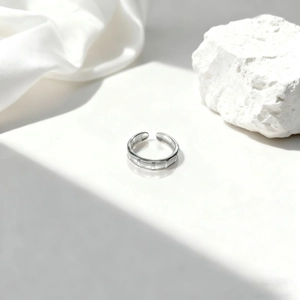 Elegante anillo abierto plateado con textura geométrica sobre fondo de seda y piedra