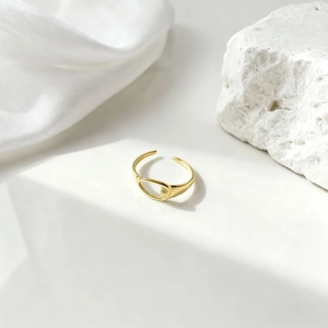 Primer plano de anillo de hoja dorado calado sobre seda blanca y piedra rugosa