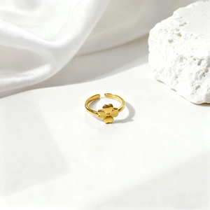 Detalle de un anillo ajustable dorado con una flor de trébol en 3D sobre fondo de seda