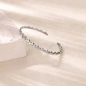 Minimalist silver open cuff bracelet with bubble-shaped edges on a stone display