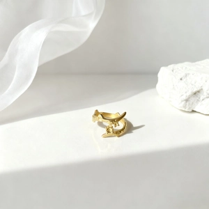 Detalle de anillo abierto dorado minimalista con textura orgánica y elegante fondo de seda