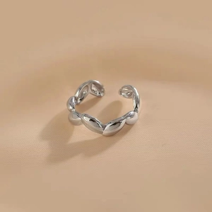 Macro de anillo abierto de ondas plateadas sobre fondo de tela beige texturizada