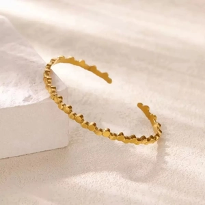 Elegant gold-plated open bangle with a hollow circular pattern on a textured stone
