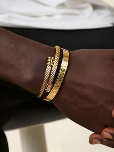 Dettaglio del set di bracciali dorati intrecciati e incisi con numeri romani al polso