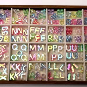 Macro view of colorful iridescent acrylic alphabet beads in a grid display box