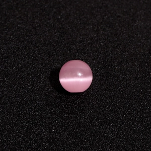 Einzelne rosa Katzenaugen-Perle mit hellem Lichteffekt auf schwarzem strukturiertem Grund