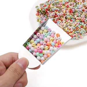 Mix of macaron colored beads in a ceramic tray with a metal scoop for DIY jewelry