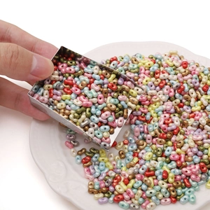 Metal shovel pouring colorful mixed oval double-hole beads into a white ceramic dish