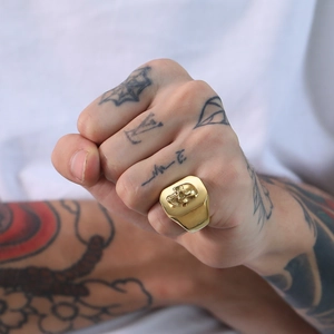 Detailed close-up of a gold punk skull signet ring on a tattooed hand for men