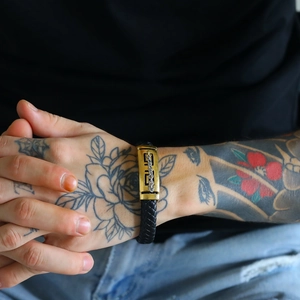 Detailed close-up of a woven cowhide leather bracelet with engraved golden curved tube