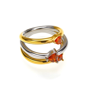 Dettaglio di tre anelli a cuore sovrapponibili in finitura oro e argento con pietre arancio