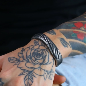 Detail of vintage gun black twisted steel cuff bracelet with hammered texture on male wrist