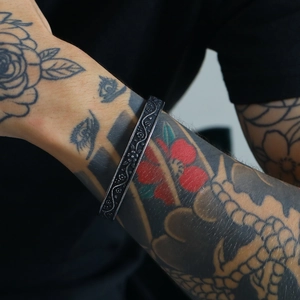 Close-up of vintage silver viking bangle with intricate floral carvings on a tattooed wrist