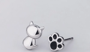 Primer plano de pendientes asimétricos de gato en plata con detalles de esmalte negro