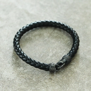 Gros plan sur un bracelet tressé en cuir noir pour homme avec fermoir gravé rétro