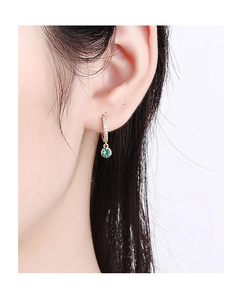 Gros plan de créoles dorées avec pavage de diamants et pendentif en zircon vert rond