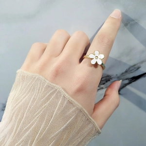Elegant gold flower ring with white petals and a crystal center worn on index finger