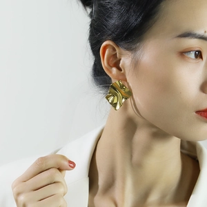 Detalle de pendientes cuadrados bañados en oro con textura ondulada en una modelo