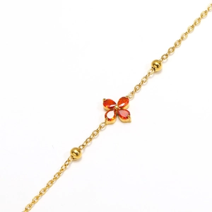 Detail of gold-plated clover bracelet with orange-red zircon stones and polished beads
