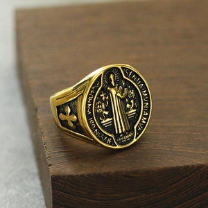 Gros plan d'une bague médaille de Saint Benoît dorée avec relief sur fond de bois sombre