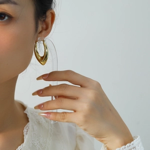Gros plan d'une boucle d'oreille géométrique dorée avec finition métal poli sur modèle