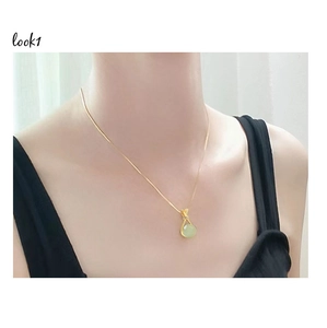 Detail view of a gold chain with a round green faux jade pendant worn by a female model