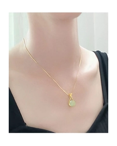 Close-up of a gold necklace with faux Hetian jade pendant worn on a female model