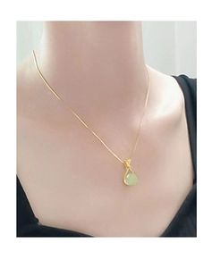 Close-up of a gold snake chain necklace with a round light green imitation jade pendant